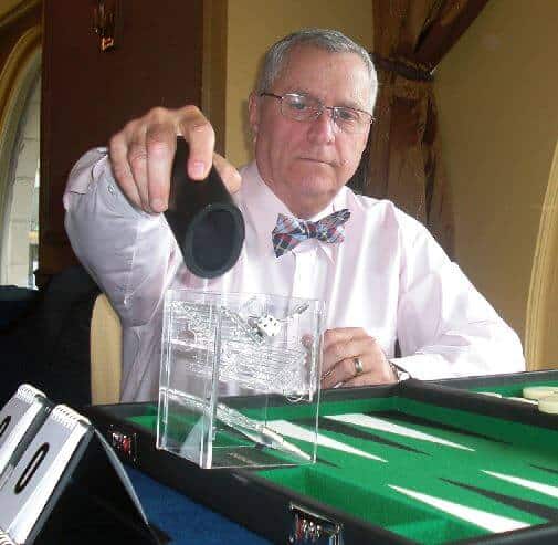 Phil Simborg in front of a backgammon board rolling dice through a baffle box.